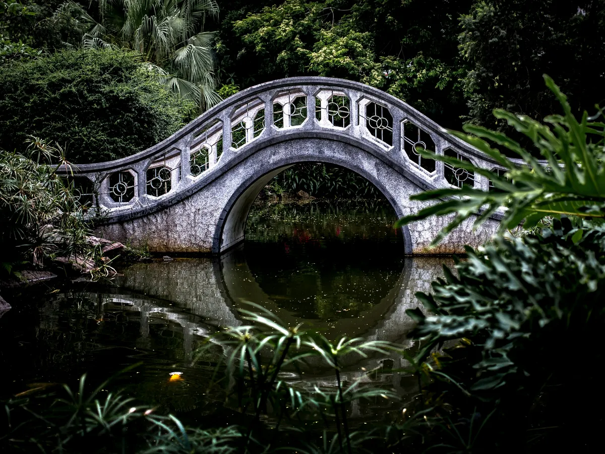 A stone moon-gate bridge arching over still water in a garden